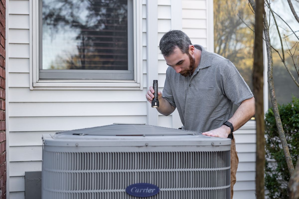HVAC technician inspecting a residential air-conditioning condenser outside a home